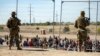 Migrantes esperan junto a una valla fronteriza bajo la vigilancia de la Guardia Nacional de Texas el 10 de mayo de 2023 para ingresar a El Paso, Texas. (AP/Andrés Leighton)