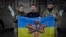 El presidente ucraniano Volodymyr Zelenskyy, en el centro, y los soldados ucranianos sostienen la bandera de una unidad militar en una posición cerca de Bakhmut, región de Donetsk, Ucrania. 